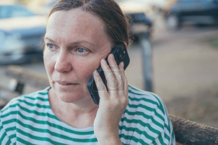 Photo for Serious concerned female talking on mobile phone outdoor on the street, selective focus - Royalty Free Image