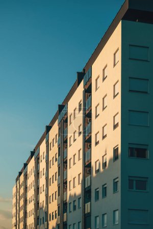 Téléchargez les photos : Immeuble d'appartements en copropriété résidentiel avec fenêtres orientées côté ouest éclairées par le soleil couchant, vue à angle bas - en image libre de droit