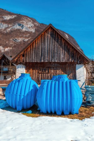 Photo for Two blue rainwater tanks in front of wooden shed in Slovenia, selective focus - Royalty Free Image