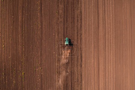 Photo for Agricultural tractor vehicle with tiller attached performing field tillage before the sowing season, aerial shot seen from the drone pov top down - Royalty Free Image