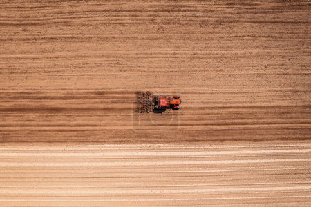 Téléchargez les photos : Tracteur agricole rouge avec tiller attaché effectuant le travail du sol avant la saison des semailles, tir aérien vu du haut vers le bas du drone pov - en image libre de droit