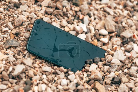 Téléchargez les photos : Smartphone humide et endommagé dans des galets de plage, mise au point sélective - en image libre de droit