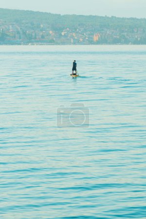 Foto de Persona irreconocible stand-up paddle boarding en el mar Adriático Golfo de Kvarner visto desde la costa de la ciudad de Crikvenica, enfoque selectivo - Imagen libre de derechos