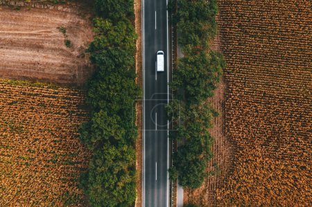 Photo for White commercial van vehicle driving along the highway road through countryside landscape, aerial shot from drone pov, directly above - Royalty Free Image
