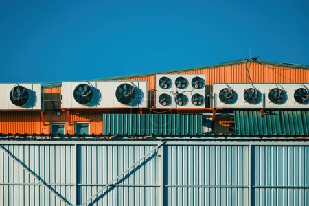 Téléchargez les photos : Entrepôt industriel avec pompes à chaleur unités externes montées sur le toit du bâtiment avec ciel comme espace de copie - en image libre de droit