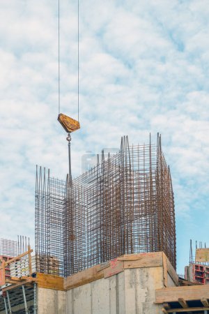 Photo for Construction crane hook lifting steel bars on building site, low angle view - Royalty Free Image