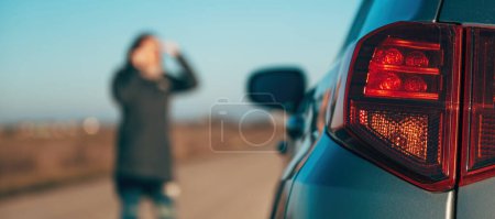 Photo for Woman making a phone call while standing by the broken down vehicle at the roadside, calling road service and maintenance mechanics, selective focus - Royalty Free Image