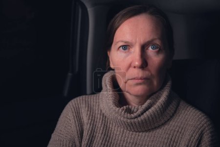 Photo for Low key portrait of serious caucasian mid adult woman at car back seat at night, looking at camera, selective focus - Royalty Free Image