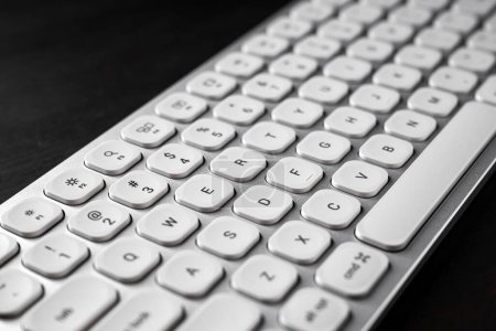 Photo for White aluminum computer keyboard on dark wooden office desk, selective focus - Royalty Free Image