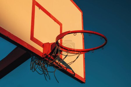 Photo for Outdoor basketball board with hoops and torn net in sunset with blue sky in background - Royalty Free Image