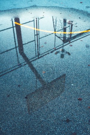 Téléchargez les photos : Réflexion du plateau de basket et des cerceaux dans un étang sur un terrain de streetball extérieur, mise au point sélective - en image libre de droit