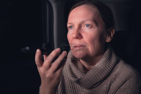 Photo for Woman talking on mobile phone from the back seat of the car while on a road trip at night, selective focus - Royalty Free Image