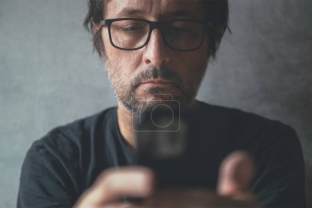 Foto de Hombre usando el teléfono celular en casa, primer plano de hombre descuidado con teléfono inteligente en las manos, enfoque selectivo - Imagen libre de derechos