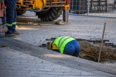 Téléchargez les photos : Travailleurs d'entretien sur place réparer les conduites d'eau endommagées sous la chaussée de la rue, mise au point sélective - en image libre de droit