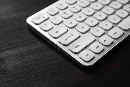 Photo for White aluminum computer keyboard on dark wooden office desk, selective focus - Royalty Free Image