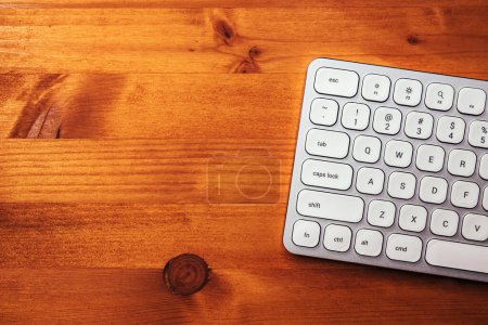 Photo for Modern white metallic personal computer keyboard on brown office desk, top view with copy space - Royalty Free Image