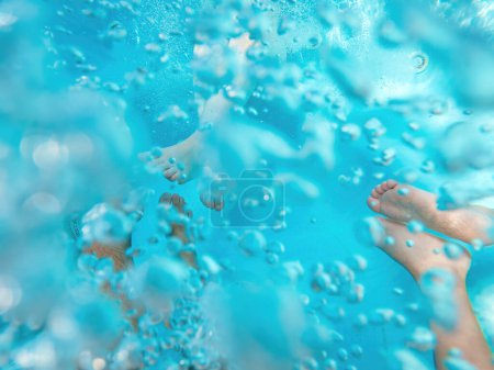 Téléchargez les photos : Famille de trois personnes dans un bain à remous, plan sous-marin des jambes dans de l'eau de piscine pétillante, mise au point sélective - en image libre de droit
