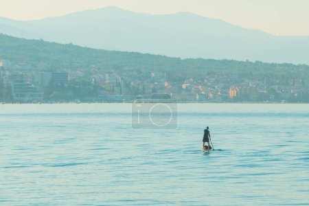 Foto de Persona irreconocible stand-up paddle boarding en el mar Adriático Golfo de Kvarner visto desde la costa de la ciudad de Crikvenica, enfoque selectivo - Imagen libre de derechos