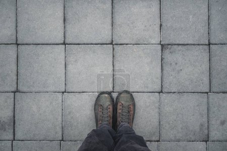 Photo for Man standing on the square shaped concrete pavement slabs, top view of dirty boots with copy space - Royalty Free Image