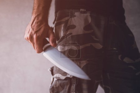 Téléchargez les photos : Homme portant un pantalon de camouflage cargo tenant un grand couteau tranchant, concept de crime et de violence, foyer sélectif - en image libre de droit