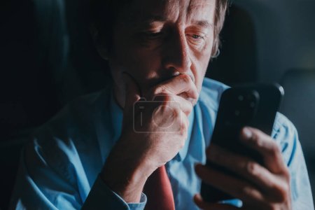 Téléchargez les photos : Un homme d'affaires utilisant un téléphone portable sur le siège arrière de la voiture rentrera du travail tard dans la nuit, discret avec une concentration sélective - en image libre de droit
