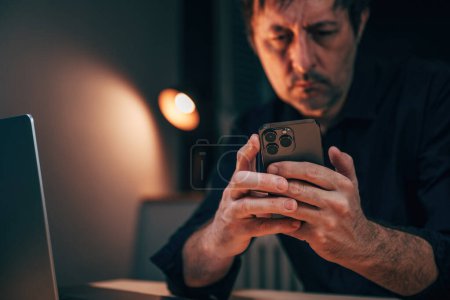 Téléchargez les photos : Homme d'affaires utilisant le téléphone portable tard dans la nuit sur son lieu de travail de l'entreprise, accent sélectif - en image libre de droit