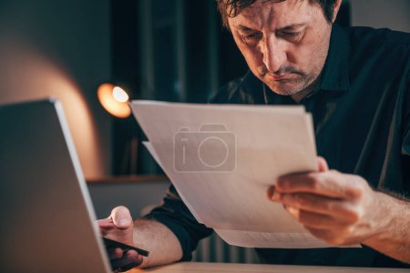 Téléchargez les photos : Homme d'affaires lisant le document de rapport papier au bureau tard dans la nuit, mise au point sélective - en image libre de droit