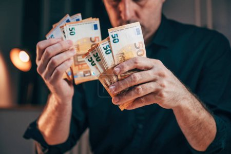 Foto de Empresario contando cincuenta billetes en euros en el cargo mientras trabaja horas extras, enfoque selectivo - Imagen libre de derechos