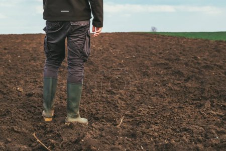 Téléchargez les photos : Agronome mâle debout dans un champ agricole labouré, vue arrière - en image libre de droit