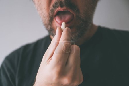 Téléchargez les photos : Homme sous traitement médical, gros plan de la main avec comprimé et bouche, mise au point sélective - en image libre de droit