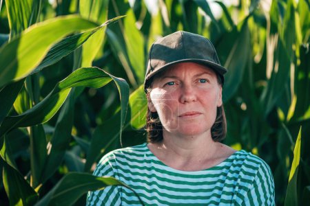 Photo for Female farmer and agronomist posing in green corn crop agricultural field and looking into distance while contemplating, selective focus - Royalty Free Image