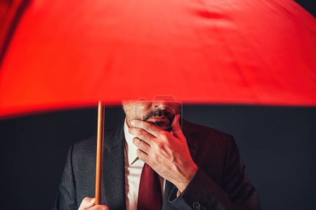 Politician holding red umbrella to protect himself, selective focus
