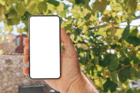 Téléchargez les photos : Homme tenant smartphone avec écran blanc blanc blanc maquette dans la cour arrière de la maison, foyer sélectif - en image libre de droit