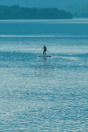 Silueta retroiluminada del deportista masculino remando tablero de pie en el lago Bohinj en Eslovenia, enfoque selectivo