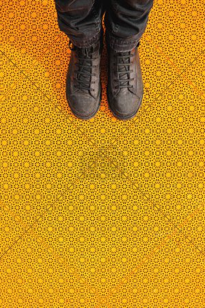 Hombre con botas viejas sucias de pie en el suelo de plástico antideslizante amarillo, vista superior