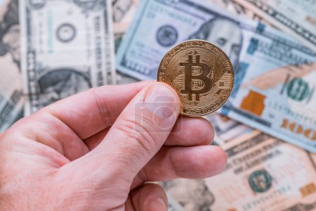 Téléchargez les photos : Trading avec Bitcoin crypto-monnaie, gros plan de la main masculine tenant pièce de monnaie sur les dollars américains, mise au point sélective - en image libre de droit