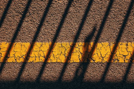 Téléchargez les photos : Surface du trottoir en asphalte avec une ligne jaune usée et un motif rayé d'ombre comme arrière-plan, vue du dessus - en image libre de droit
