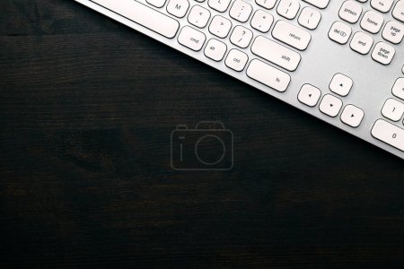Photo for Modern white aluminum computer keyboard on dark wooden home office desk as copy space, top view - Royalty Free Image