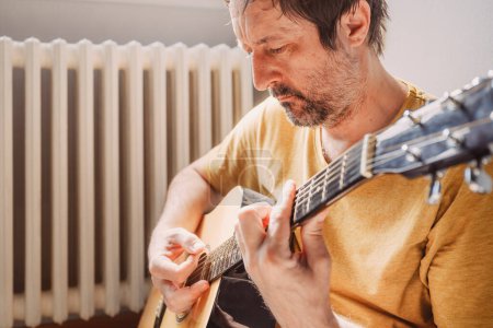 Téléchargez les photos : Solitaire mi adulte mâle jouant de la guitare acoustique à la maison, foyer sélectif - en image libre de droit