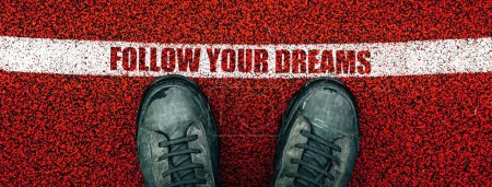 Photo for Follow your dreams text on rubber playground flooring, male boots from above standing next to the line, directly above - Royalty Free Image