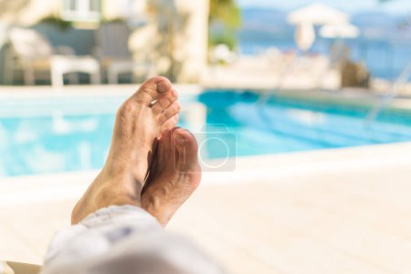 Foto de Descalzo turista masculino relajándose junto a la piscina al aire libre en el balneario en el soleado día de verano, pov shot con enfoque selectivo - Imagen libre de derechos