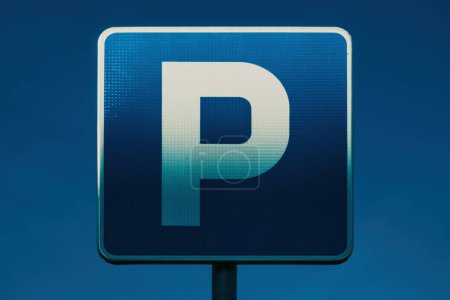 Parking area blue sign with white letter P illuminated by the warm sunset light, selective focus
