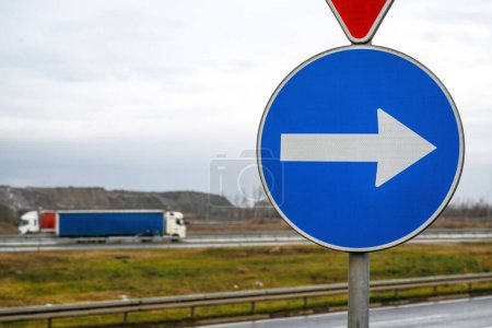 Téléchargez les photos : Signe de direction obligatoire sur l'autoroute avec deux semi-camions en arrière-plan, mise au point sélective - en image libre de droit