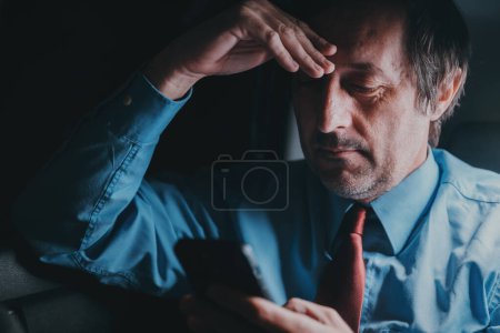 Téléchargez les photos : Un homme d'affaires utilisant un téléphone portable sur le siège arrière de la voiture rentrera du travail tard dans la nuit, discret avec une concentration sélective - en image libre de droit