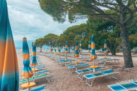 Folded beach umbrellas and empty deck chairs on town beach in Crikvenica, Croatia. Overcast weather and cloudy days during poor touristic season, selective focus