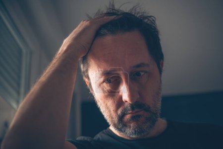 Photo for Disappointed adult caucasian male looking down in dark room, selective focus - Royalty Free Image