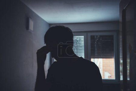 Foto de Silueta de hombre triste deprimido en habitación oscura con persianas tiradas hacia abajo, enfoque selectivo - Imagen libre de derechos