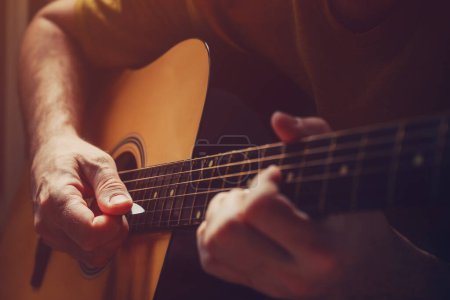 Téléchargez les photos : Homme jouant de la guitare acoustique à la maison, image discrète avec mise au point sélective - en image libre de droit