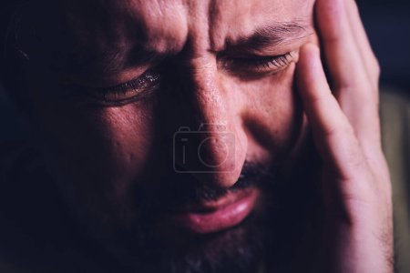 Foto de Desesperanza y desesperación, primer plano del retrato del triste hombre adulto llorando afligido en la habitación oscura, enfoque selectivo - Imagen libre de derechos