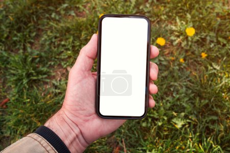 Foto de Smartphone maqueta, mano masculina sosteniendo el teléfono móvil con pantalla blanca en blanco en el parque en la mañana de primavera, enfoque selectivo - Imagen libre de derechos